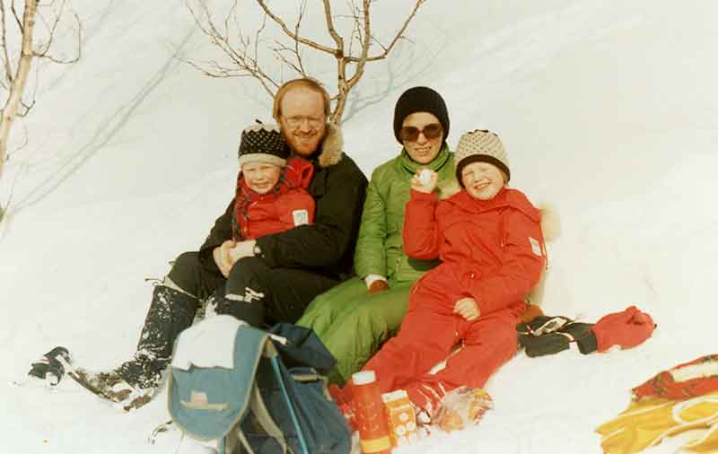 1970's Norwegian Family Of Four Take A Break Together Smiling Sitting On Snow In Colorful Snowsuits.