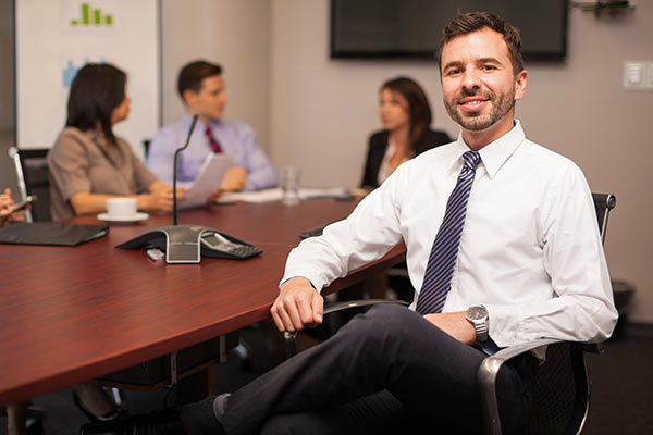 Man Smiling In Business Office Boardroom With Managers Meeting Behind Him Discussing Website Video Online Advertising
