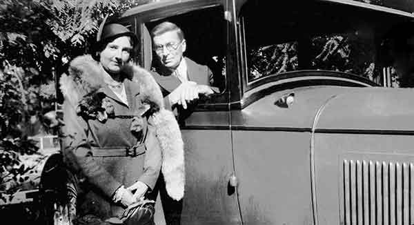 Woman With Fox Wrapped Around Her Neck Standing Beside Man Leaning Out Of 1927 Studebaker Car
