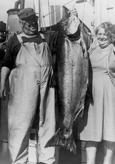 Older Fisherman Hangs Huge Chinook Spring Salmon At Dock Smiling Woman Watching Rivers Inlet Late 1940's