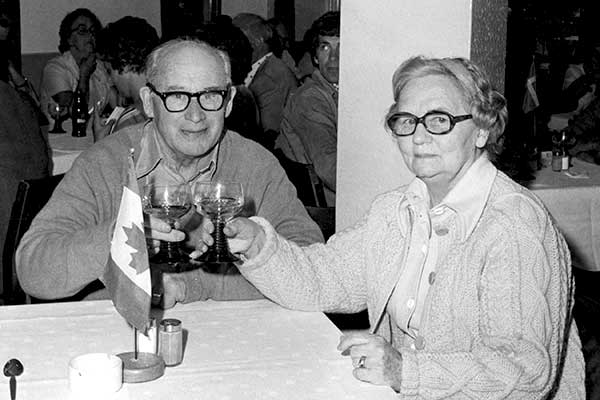 Senior Couple In Love Raise Wine Glasses To Toast Cheers At Restaurant Canadian Flag On Table